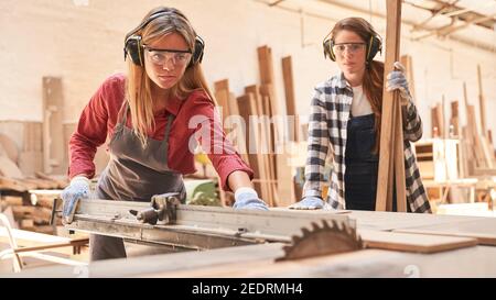 Two young women as carpenter apprentices work on the circular saw in the workshop Stock Photo