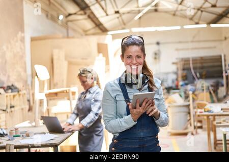 Smiling craftsman woman in carpentry workshop using tablet computer Stock Photo
