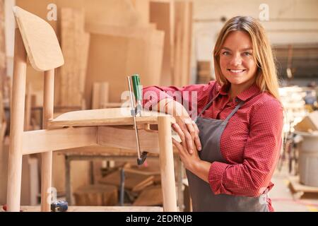 Young woman as a carpenter apprentice gluing chair in the cabinet making Stock Photo