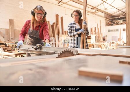 Woman as a craftsman trainee works on the circular saw of the joinery workshop Stock Photo