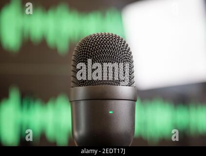 Digital microphone, sound for audience. Mic condenser black metallic, blur green waveform background. Sound recording concept. Mike for live audio, mu Stock Photo