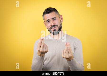 Handsome man with beard wearing sweater over yellow background doing money gesture with hands, asking for salary payment, millionaire business Stock Photo