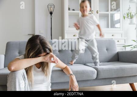 Hyperactive child and his tired and sad mother at home Stock Photo