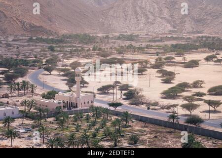 Small mosque in the rural area of Musandam province Suburbs of Bukha village, Oman. Palm trees in the desert under steep mountains. Stock Photo