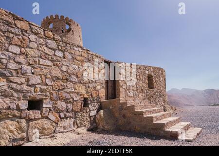Stone wall of a small medieval arabian fort with wooden door and stone stairs in Bukha, Oman. Stock Photo