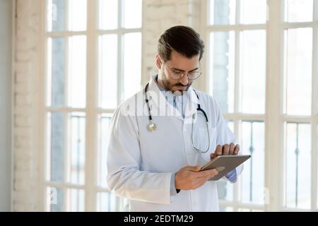 Focused young male doctor using electronic digital touchscreen gadget. Stock Photo