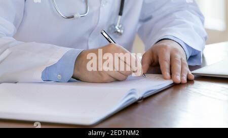 Close up male doctor writing notes in registry book. Stock Photo