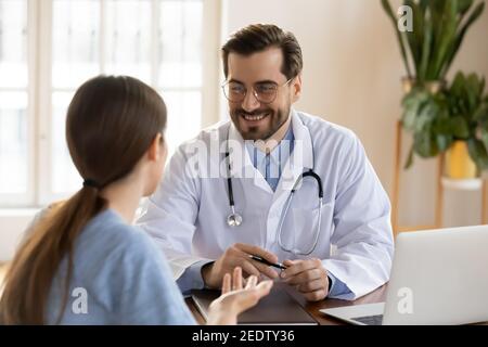 Smiling young male general practitioner in uniform listening to woman. Stock Photo