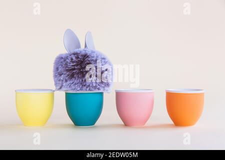 Fur ball with bunny rabbit ears in egg stand on bright background. Four egg stands. Easter minimal concept. Close-up, postcard Stock Photo