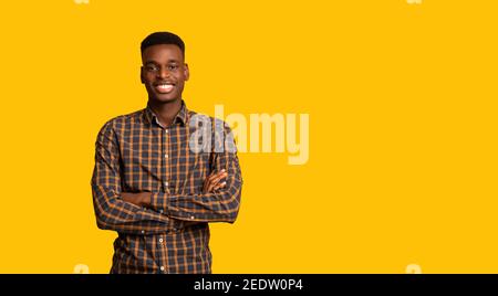 Positive Young Black Guy Posing With Folded Arms Over Yellow Studio Backgound Stock Photo