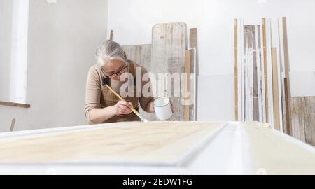 wood crafts, woman artisan carpenter painting with brush and paint jar white the door in workshop, wearing overall and eyeglasses, interior designer, Stock Photo