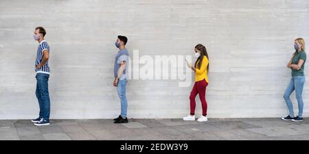 Young people from different cultures and race waiting in queue outside shop market while keeping social distance Stock Photo