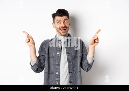 Happy stylish guy laughing and pointing sideways, showing two choices, demonstrate promo offers and smiling, standing against white background Stock Photo