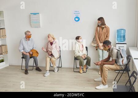 Wide angle view at hospital waiting room with diverse group of people waiting in line for vaccination, copy space Stock Photo