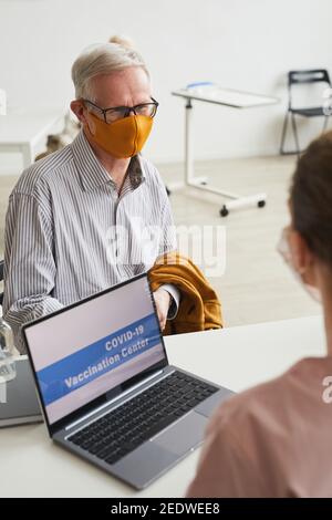 Vertical portrait of white haired senior man wearing mask while registering for covid vaccine at medical center, copy space Stock Photo