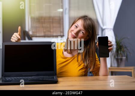 The woman uses a laptop and a smartphone with a blank black screen at home. Template for your look. Black mock up gadgets screen Stock Photo