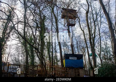 Wendover, Buckinghamshire, UK. 15th February, 2021. Tree houses at the nearby Stop HS2 Wendover camp. HS2 Ltd have this morning fenced off a public footpath and started fencing off an area of woodland known as the Spinney in readiness to fell numerous mature trees as part of the High Speed 2 rail link from London to Birmingham. The landowner was allegedly not notified by HS2 Ltd in advance. National Eviction Team (NET) bailiffs working for HS2 were on site as were a large number of police who were using a drone above the woods. Anti HS2 activists are living in the woods nearby in an attempt to Stock Photo