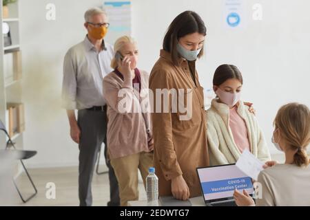 Diverse group of people waiting in line while registering for covid vaccine in medical center, copy space Stock Photo