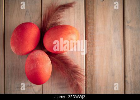 Three orange easter eggs and feathers on a wooden background. Place for your text. Stock Photo