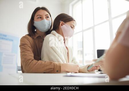 Low angle portrait of mother and daughter registering for covid vaccination in medical clinic, copy space Stock Photo