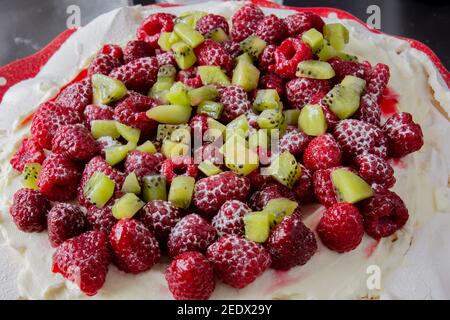 Pavlova, meringue cake preparation, mascarpone cream and kiwi, raspberry covered, New Zealand Australian dessert Stock Photo