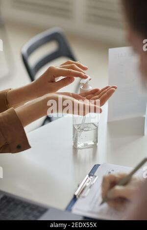 Vertical close up of unrecognizable woman using hand sanitizer at doctors office, copy space Stock Photo