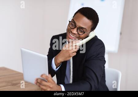 Black man in suit talking on phone, using digital tablet Stock Photo