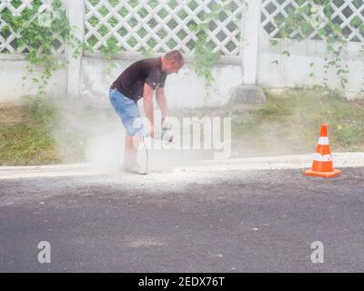 Russia, Sochi 01.07.2020. A man works with saw with a grinder in the clouds of rising dust on the side of an asphalt road Stock Photo