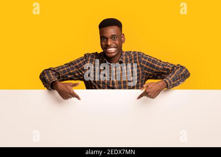 Free Place For Ad. Cheeful Black Guy Pointing Down At White Board Stock Photo