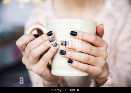 girl hands holding a cup of coffee with beautiful black manicure. Christmas and Stock Photo