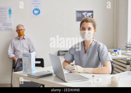 Portrait of young female doctor wearing mask and looking at camera while waiting for patients in clinic or vaccination center, copy space Stock Photo