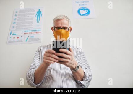 Low angle portrait of w white haired senior man using smartphone while waiting in line at medical clinic, copy space Stock Photo