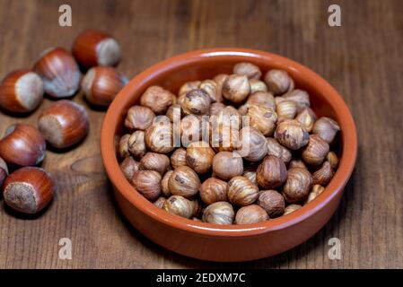 Peeled hazelnuts in bowl and hazelnuts in shell on rustic wooden table Stock Photo