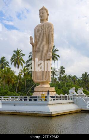 HIKKADUWA, SRI LANKA - FEBRUARY 14, 2020: A giant sculpture of a standing Buddha equal in height to the wave of tsunamis that destroyed the coast of S Stock Photo