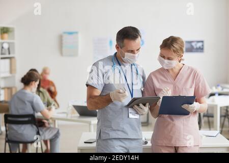 Waist up portrait of two doctors wearing masks and talking while looking at tablet in medical clinic, copy space Stock Photo