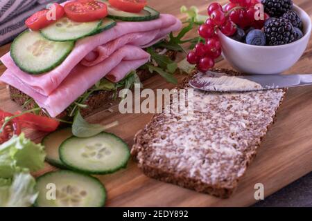 Open sandwich with ham, tomatoes and cucumbers served with fresh berries on a wooden board Stock Photo