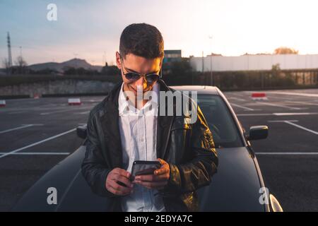 Young caucasian man using a smartphone with a sports car behind Stock Photo