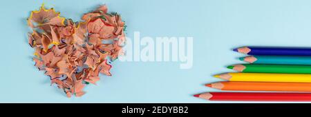 Banner with sharpened colored pencils and heart-shaped pencil shavings on pastel blue color. Rainbow or LGBT pencils. Decoration for St. Valentine's Day. Top view Stock Photo