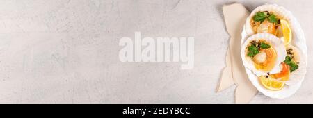 Banner with baked scallops with caviar and creamy garlic sauce in white plate. Scallops with lemon on white background with napkin. Top view. Copy space. Flat lay Stock Photo