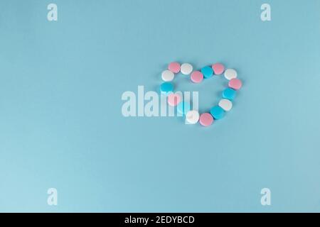 Medicines and pills. Heart-shaped blue, pink and white pills. Multicolored medicines on a pastel blue background. Stock Photo