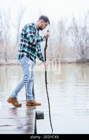 BeardHispanic man wearing flannel holding a wooden stick in the lake Stock Photo