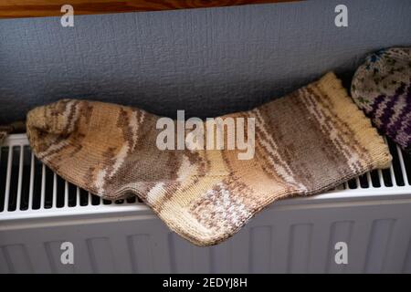 Light brown hand knitted socks on hot white radiator. How to dry knitted socks. How to wash natural knitted socks. Stock Photo