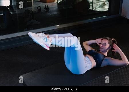 Beautiful young woman doing abs crunches in gym. Getting perfect body shape and losing weight requires lots of stamina. Healthy life concept. Stock Photo