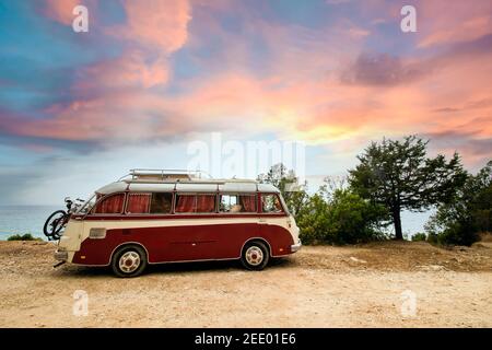 A Volkswagen T2 is parked on seafront promenade in Sardinia during a stunning sunset. Stock Photo