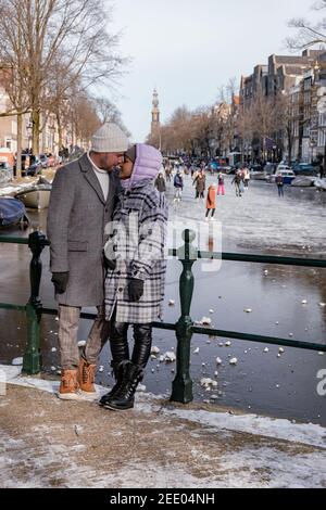 couple visit Amsterdam during Winter with people Ice skating on the canals in Amsterdam the Netherlands in winter, frozen canals in Amsterdam during winter.  Stock Photo