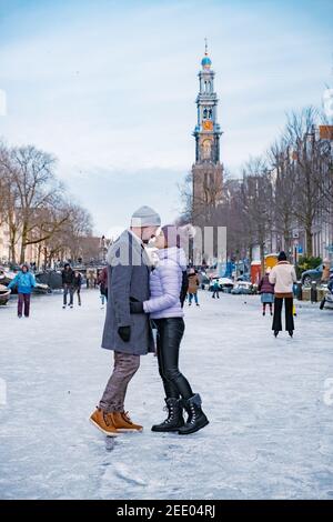 couple visit Amsterdam during Winter with people Ice skating on the canals in Amsterdam the Netherlands in winter, frozen canals in Amsterdam during winter.  Stock Photo