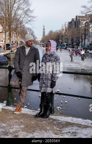 couple visit Amsterdam during Winter with people Ice skating on the canals in Amsterdam the Netherlands in winter, frozen canals in Amsterdam during winter.  Stock Photo