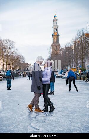 couple visit Amsterdam during Winter with people Ice skating on the canals in Amsterdam the Netherlands in winter, frozen canals in Amsterdam during winter.  Stock Photo