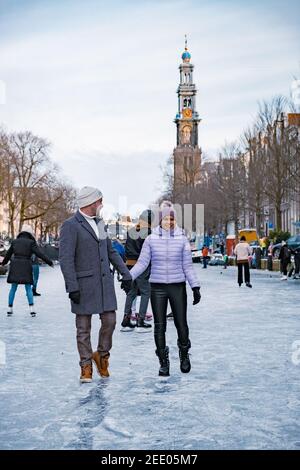 couple visit Amsterdam during Winter with people Ice skating on the canals in Amsterdam the Netherlands in winter, frozen canals in Amsterdam during winter.  Stock Photo