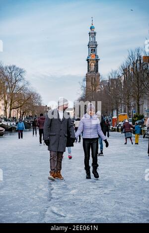 couple visit Amsterdam during Winter with people Ice skating on the canals in Amsterdam the Netherlands in winter, frozen canals in Amsterdam during winter.  Stock Photo